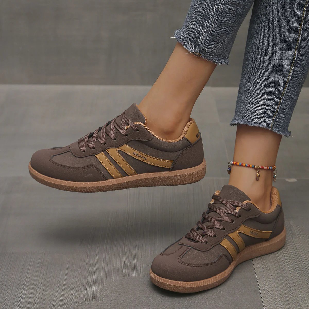 A woman wearing off-white Elara orthopaedic cushioned trainers, walking outdoors on a paved path, showcasing comfort.