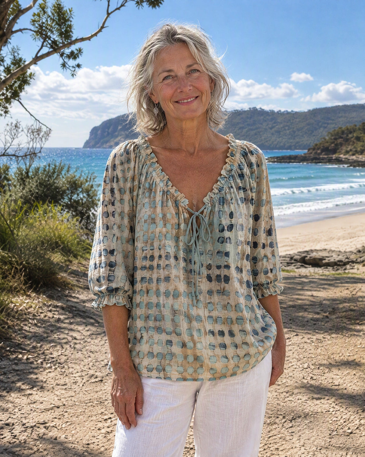 Front view of a teal Fiona blouse featuring its soft polka dot print and ruffled tie-neck design.
