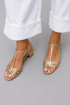 Pair of Allegra vintage sandals in gold color on a light background, top view.
