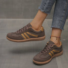 A woman wearing off-white Elara orthopaedic cushioned trainers, walking outdoors on a paved path, showcasing comfort.