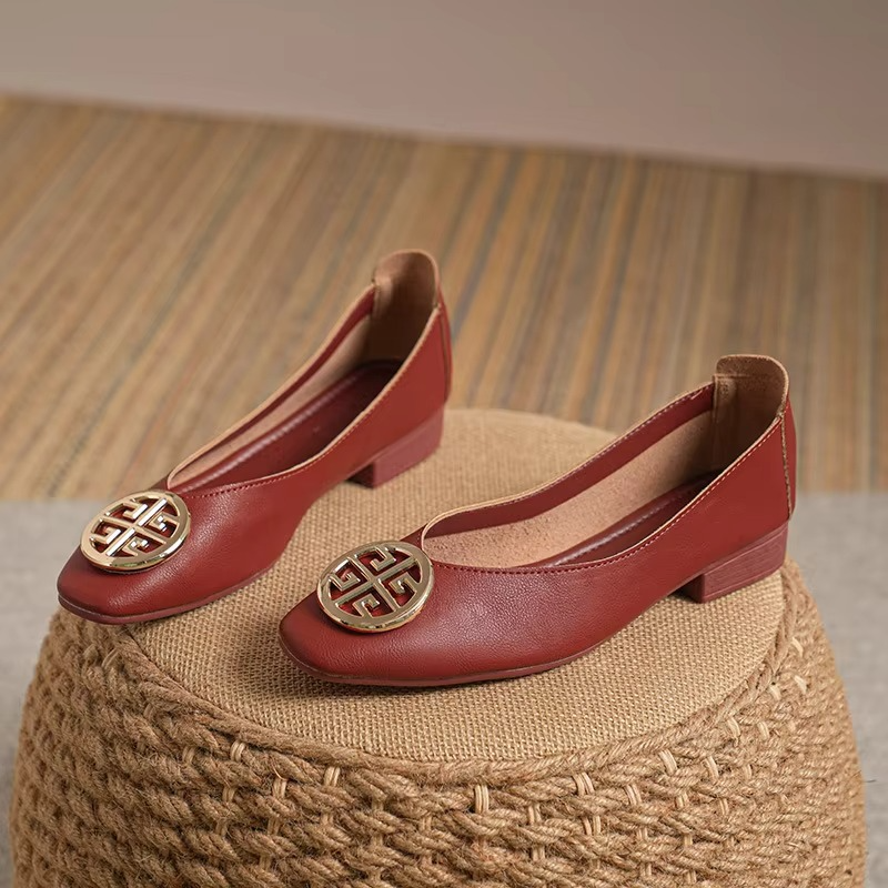 Close-up of the gold circular accent on red square-toe flats, highlighting the polished hardware.