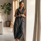 Side profile of the olive green sleeveless jumpsuit, highlighting the dropped-crotch wide-leg silhouette and rolled ankle cuff.