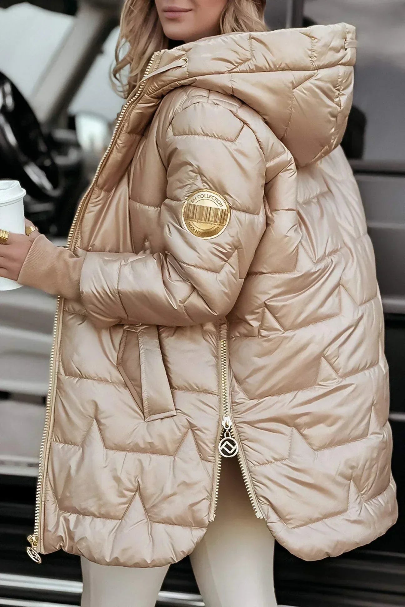Woman zipping up a beige hooded winter jacket, showing the functional zipper and side pockets.