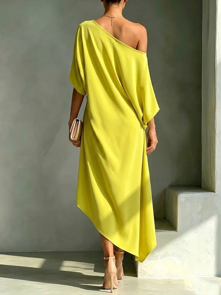 Back view of a blue asymmetrical midi dress, revealing the gentle flow of the dipped hem and the refined contemporary design.